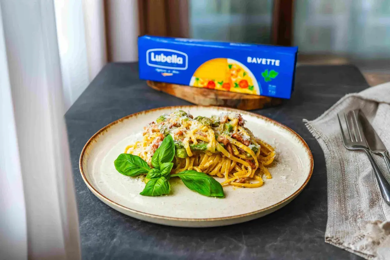 Pyszna carbonara ze szparagami na talerzu, udekorowana bazylią. Obok opakowanie makaronu Lubella Bavette.