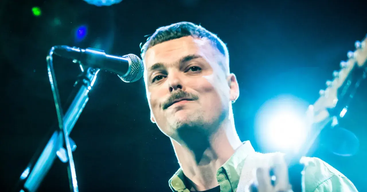 Blazej Krol śpiewa do mikrofonu, trzymając gitarę.