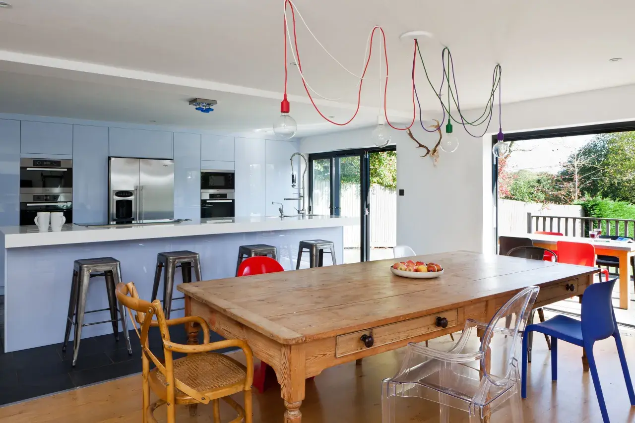 Un affascinante abbinamento sedie Kartell con tavolo antico in legno, circondato da una cucina moderna e un giardino lussureggiante.