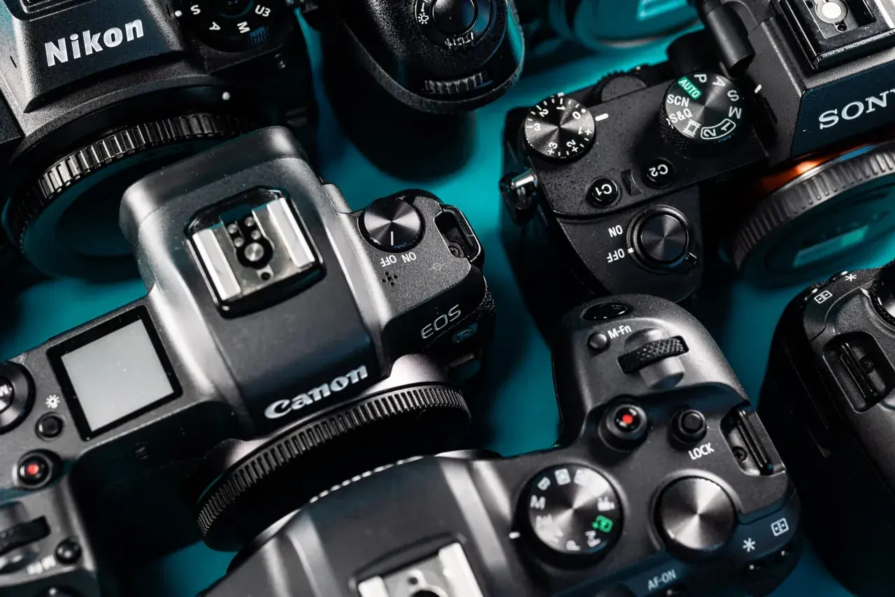 Zbliżenie na kilka aparatów fotograficznych marek Nikon, Canon i Sony, ułożonych na niebieskim tle.