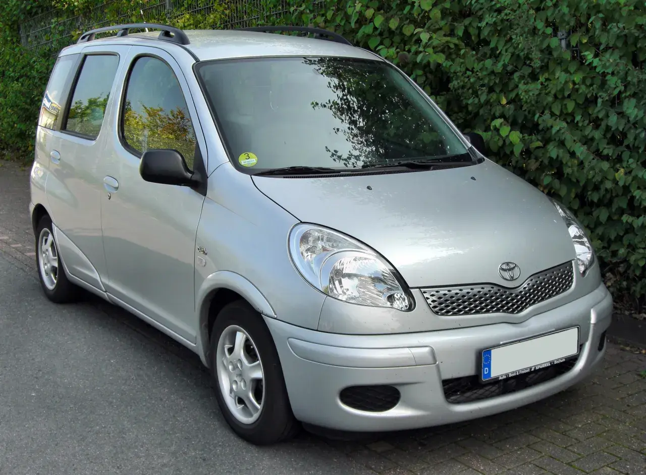 Srebrny Toyota Yaris Verso stoi na tle zielonych krzewów.