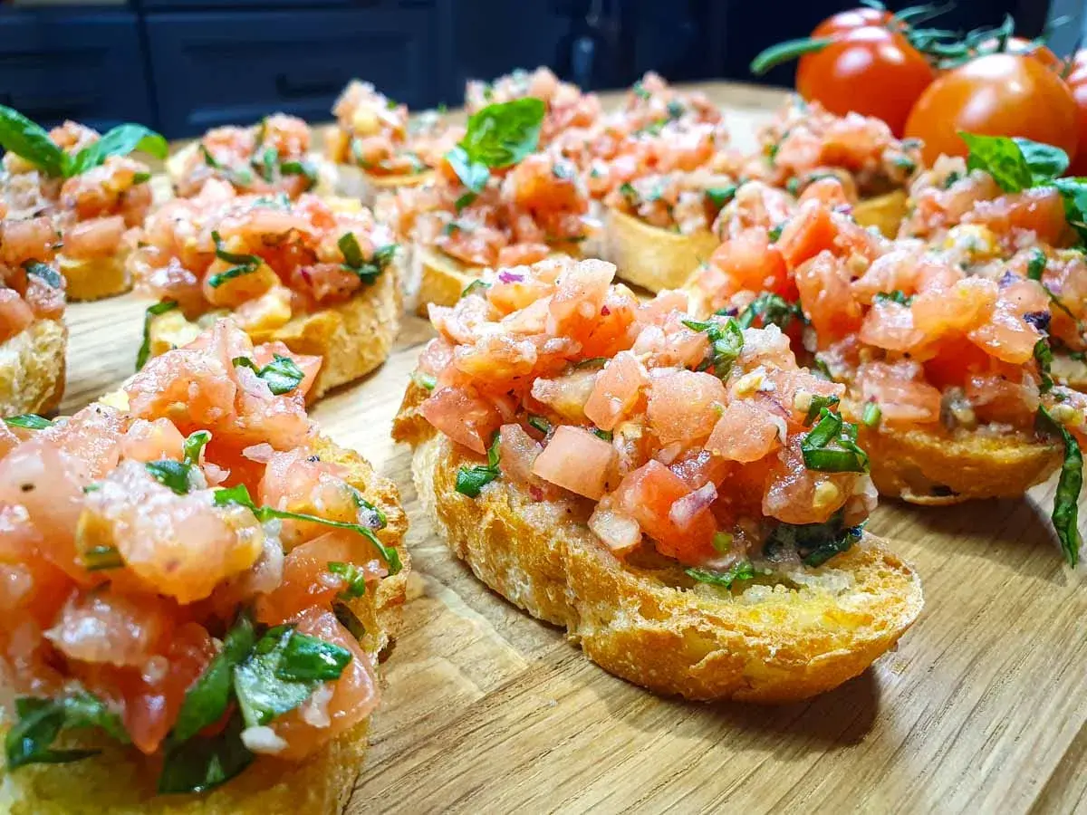Pyszne bruschetta z pomidorami i bazylią, ułożone na drewnianej desce. Idealna przekąska na lato.