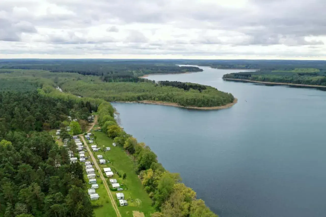 Vue aérienne d'un camping naturiste en Allemagne, bordé par une forêt dense et un lac paisible.