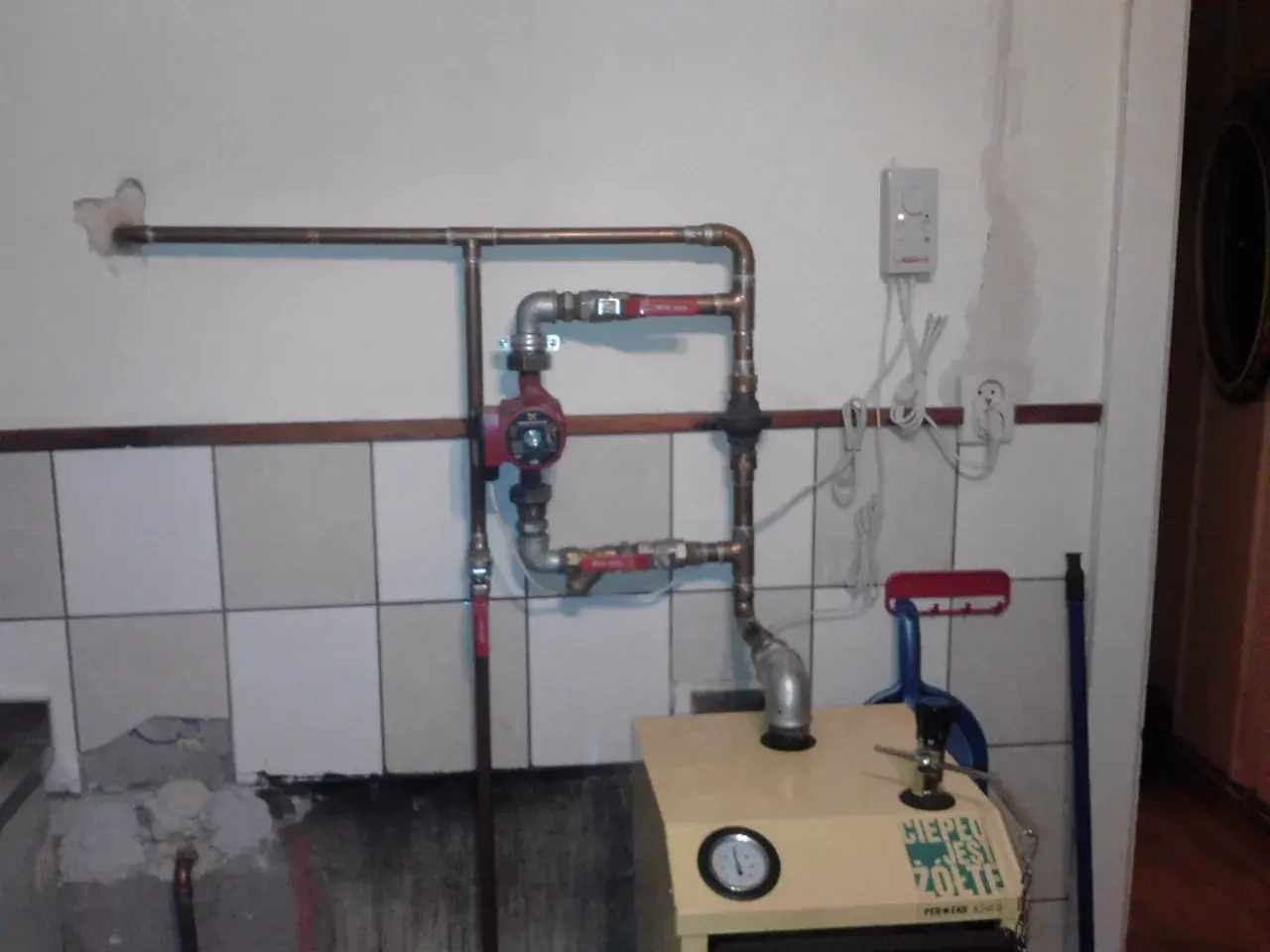 Montaż pompy CO w układzie otwartym. Widoczna instalacja miedziana, czerwona pompa obiegowa, zawory i fragment kotła.