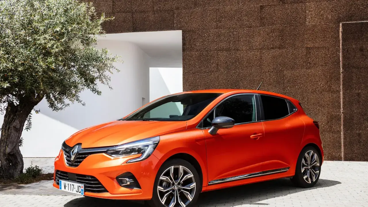 En orange Renault Clio 2026 parkerad vid en modern byggnad med en olivträd i förgrunden.