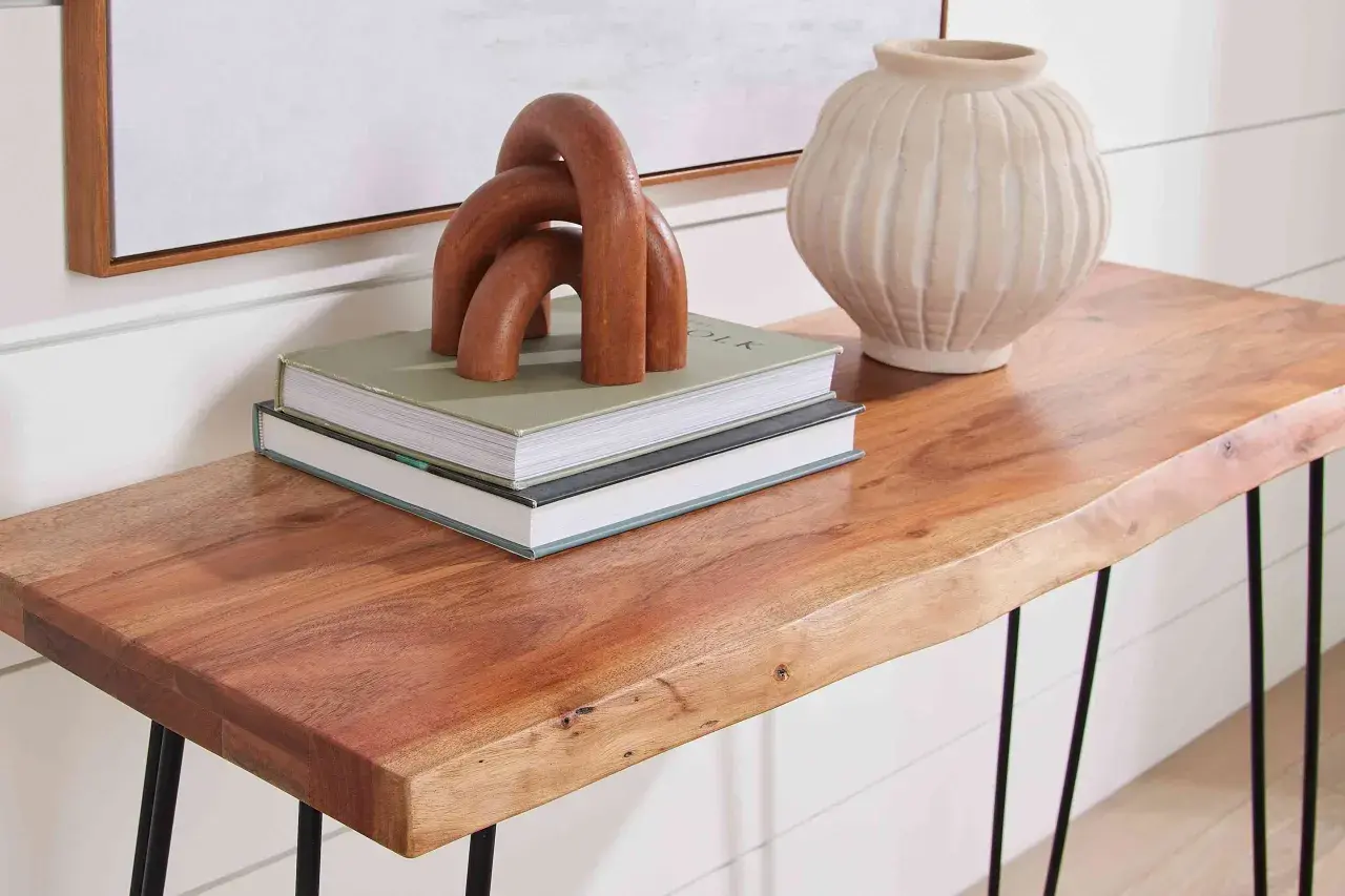 A live-edge acacia hardwood console table displays books, a wooden sculpture, and a textured vase.