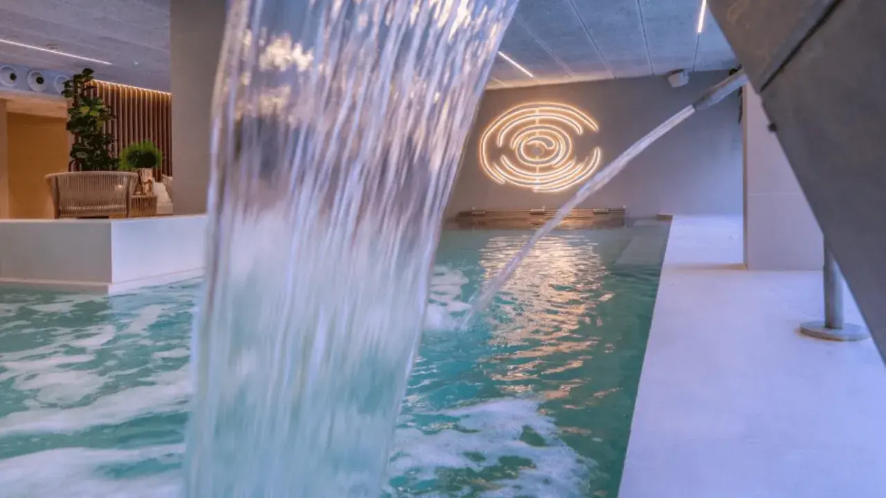 Cascada de agua en piscina interior, con iluminación circular y zona de descanso. Un oasis de spa sol y mar en Calpe.
