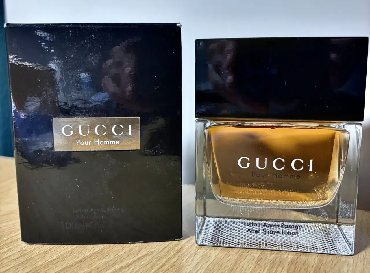 Elegancki zestaw z wodą po goleniu Gucci Pour Homme. Złocisty płyn w szklanym flakonie i czarne opakowanie.