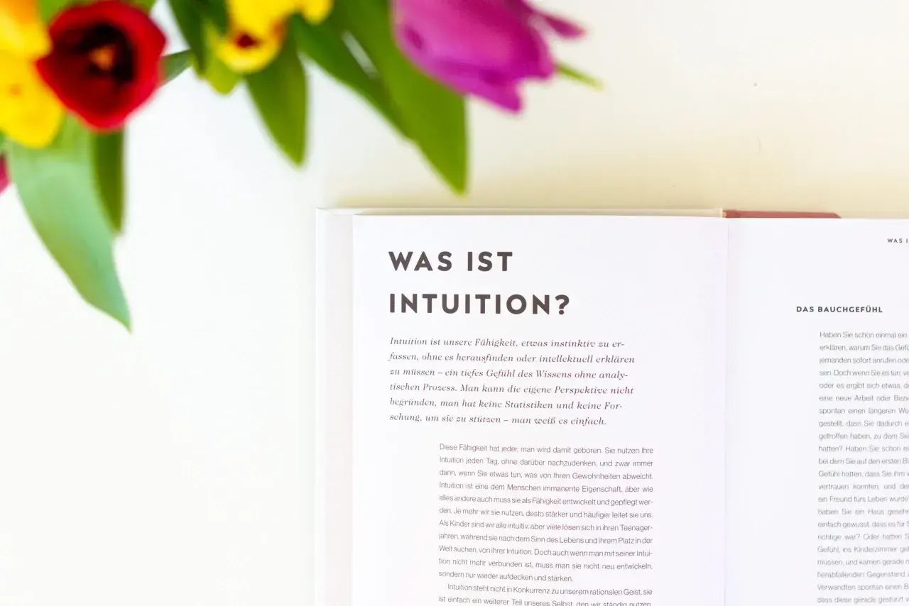 Blumen und ein Buch über Intuition. Lerne, deine Intuition zu trainieren und dem Bauchgefühl zu vertrauen.