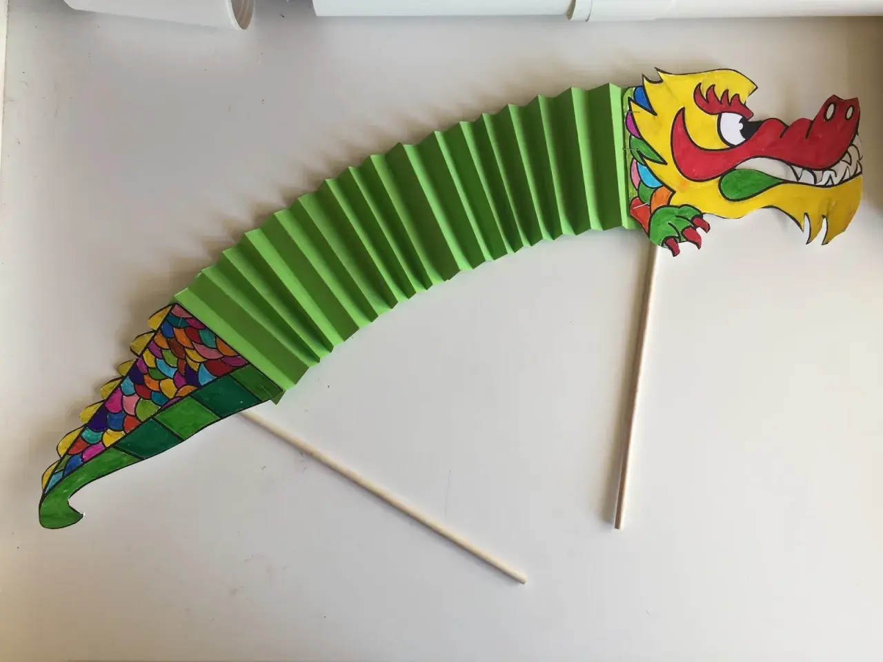 Dragón de papel verde, parte de un manualidades proyecto china infantil. Cabeza colorida y cuerpo en acordeón.
