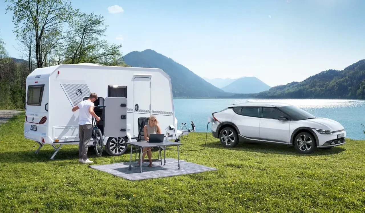 Para wakacyjna z przyczepą kempingową i ładowanym autem elektrycznym nad jeziorem. Idealne na wycieczkę z prawem jazdy B96.