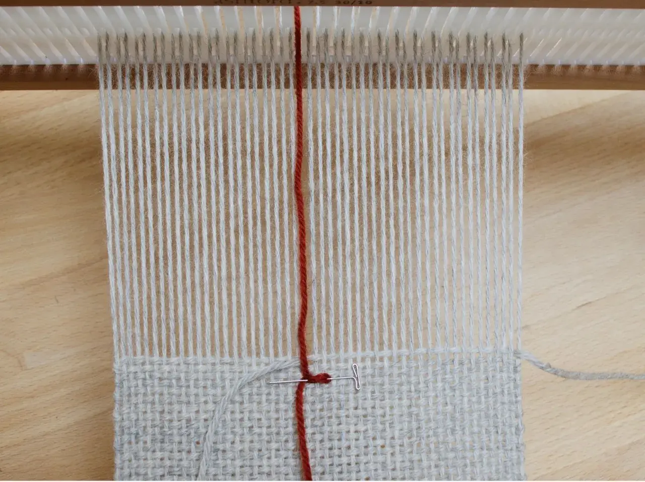 Début d'un tissage sur métier, fils de coton gris et rouge. La technique de tissage se révèle avec chaque passage.