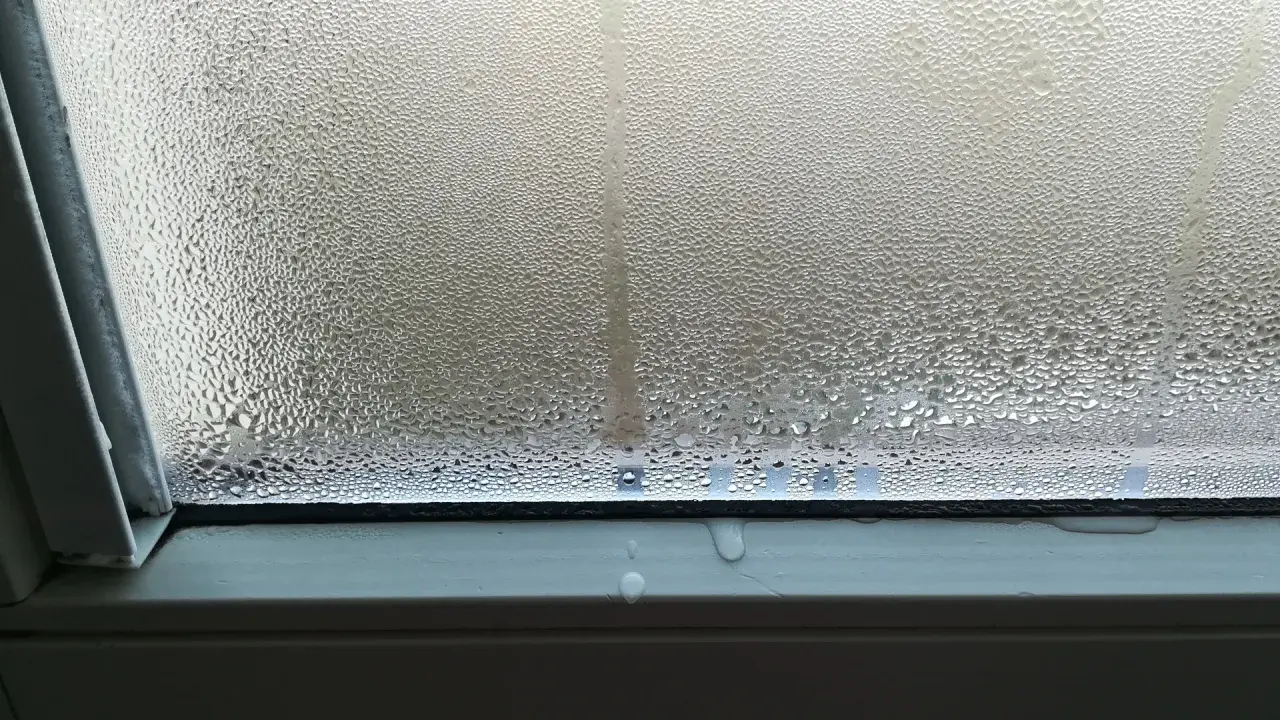 Goccioline d'acqua su un vetro, un fenomeno che illustra il concetto di traspirante significato, con condensa che scivola sul davanzale.