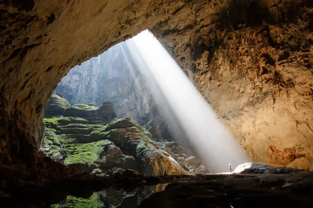 Promień słońca wpada do jaskini Son Doong, oświetlając zielone mchy i skalne tarasy.