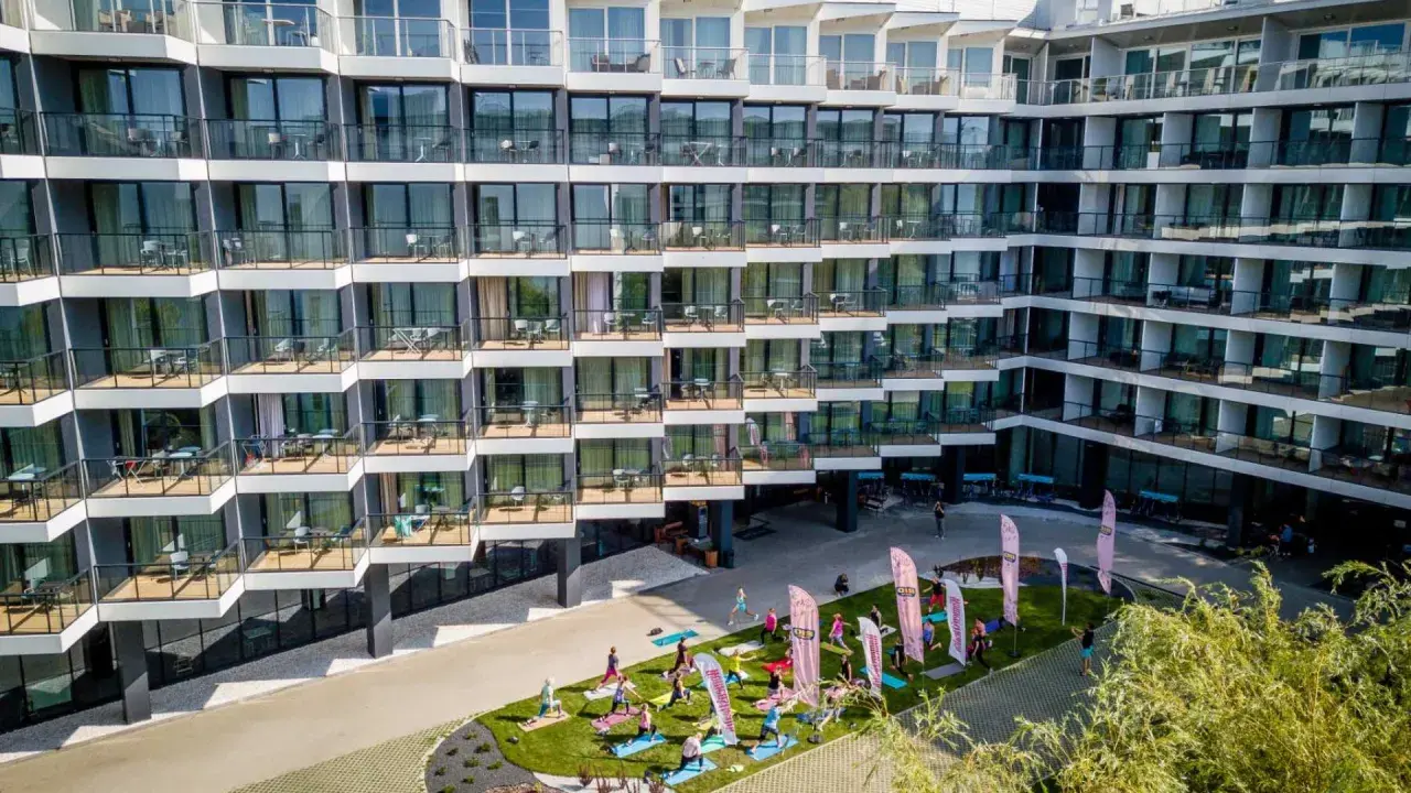 Grupa osób ćwiczy jogę na trawniku przed nowoczesnym seaside park hotel.