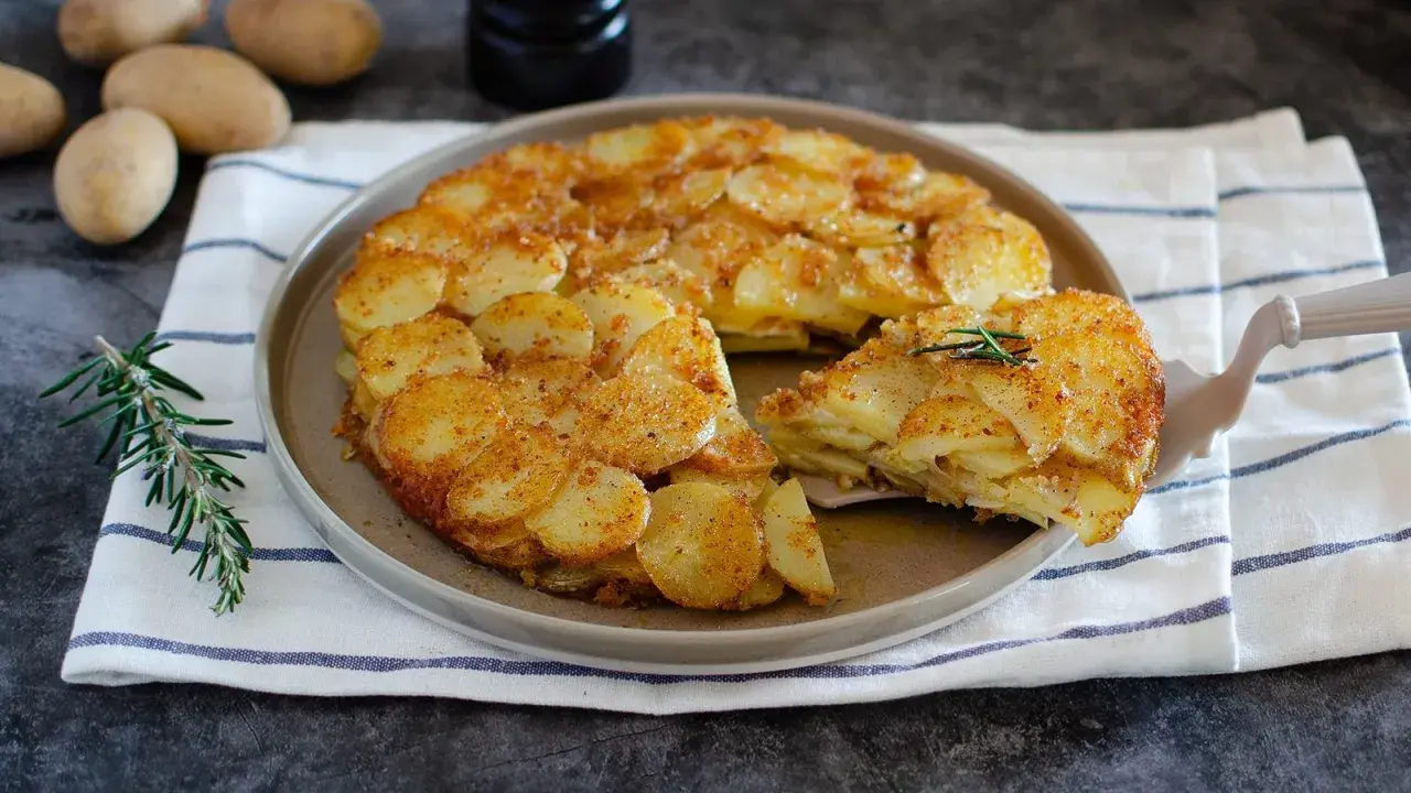 Un delizioso tortino di patate dorato e croccante, servito su un piatto con rosmarino fresco.