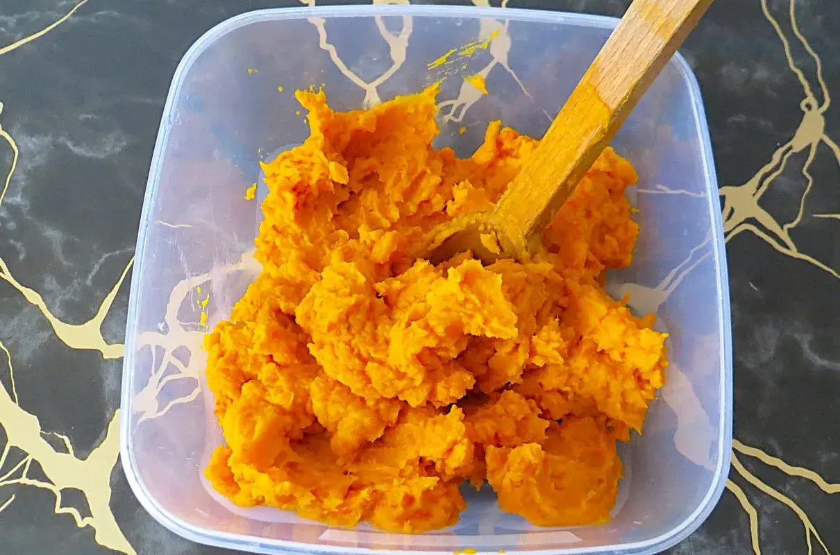 Jasne, oto opis:

Pomarańczowe, gęste puree z dyni hokkaido w plastikowym pojemniku, z drewnianą łyżką.