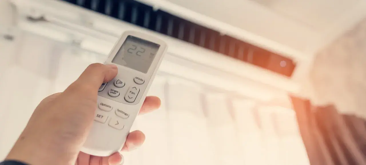 Mano ajustando el control remoto del aire acondicionado, mostrando la temperatura a 22 grados. ¿Qué potencia de aire acondicionado necesito para mi hogar?