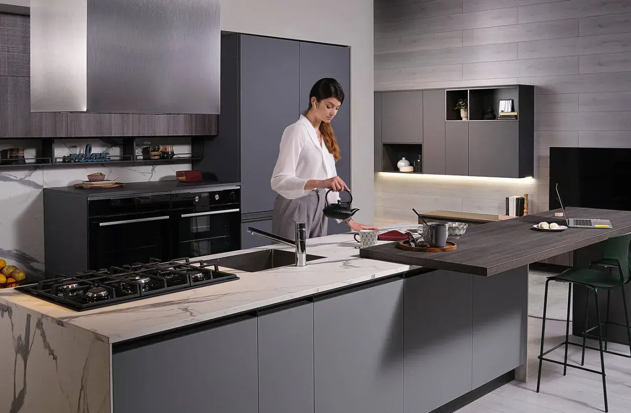 Donna prepara il tè in una moderna isola cucina fai da te con piano in marmo e bancone snack.
