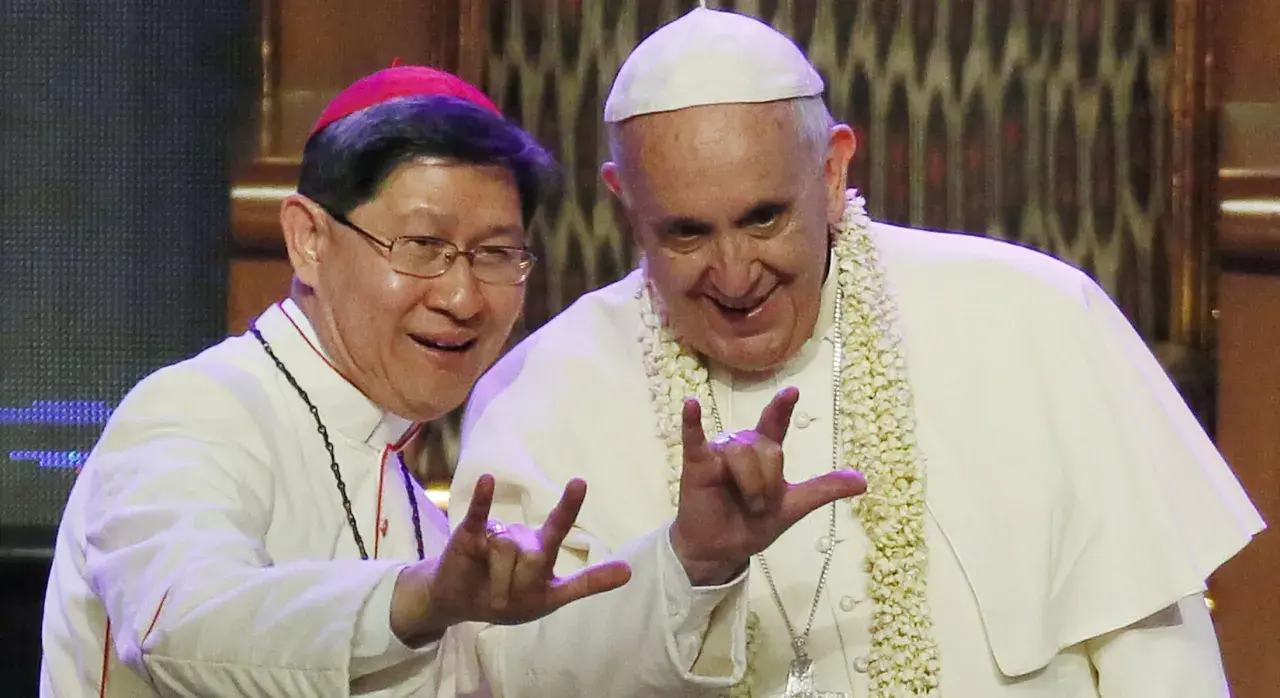 Papa Francesco e un vescovo fanno il gesto delle corna a tre dita, un segno di benedizione e speranza.