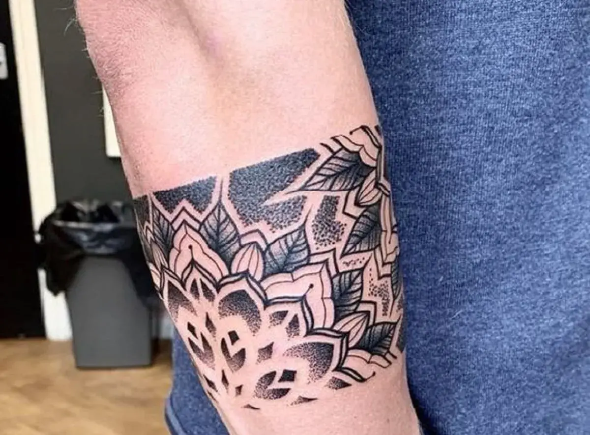 Eleganckie tatuaże męskie na ramieniu w stylu mandali, z motywami liści i geometrycznymi wzorami, wykonane techniką dotwork.