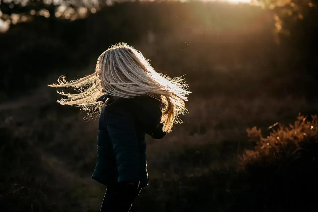 Dziecko z rozwianymi blond włosami w świetle zachodzącego słońca.