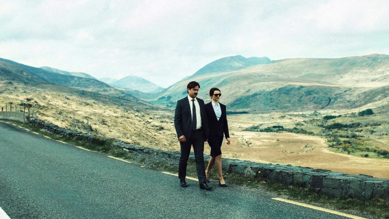 Coppia in abito cammina su strada panoramica, paesaggio montuoso. Un'immagine che evoca la recensione di "The Lobster".