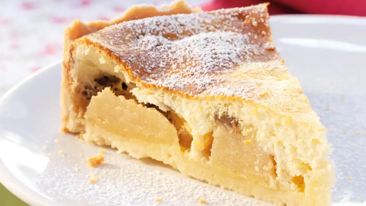 Ein Stück Apfelkuchen mit Quark, bestäubt mit Puderzucker, auf einem weißen Teller.