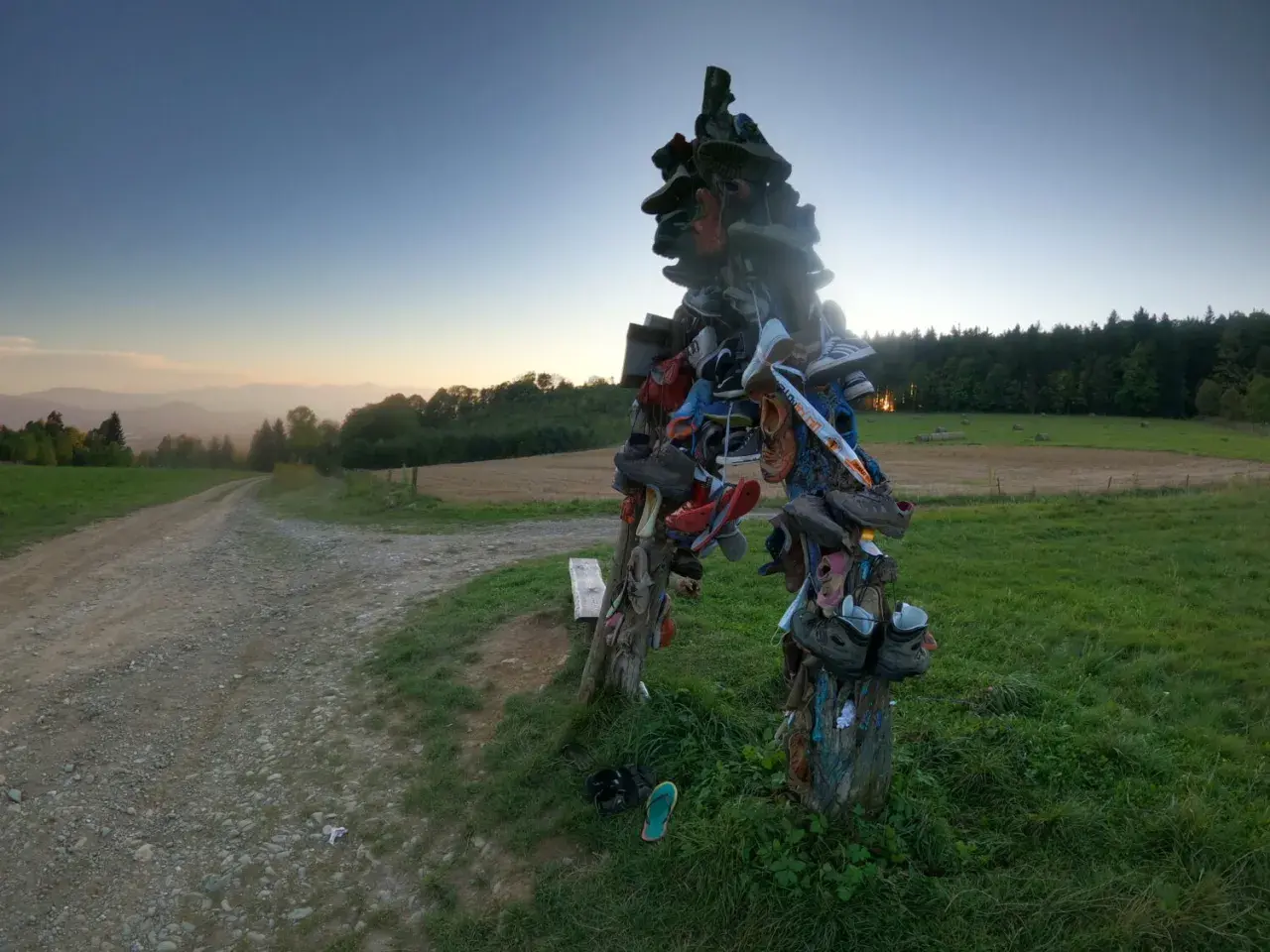 Skopiec szczyt. Rzeźba z butów na szczycie wzgórza, obok polnej drogi, o zachodzie słońca.