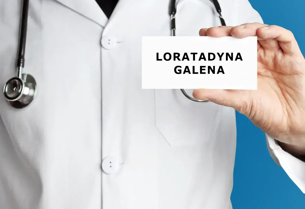 Lekarz trzyma kartkę z napisem "LORATADYNA GALENA". Stetoskop wisi na jego białej katanie.