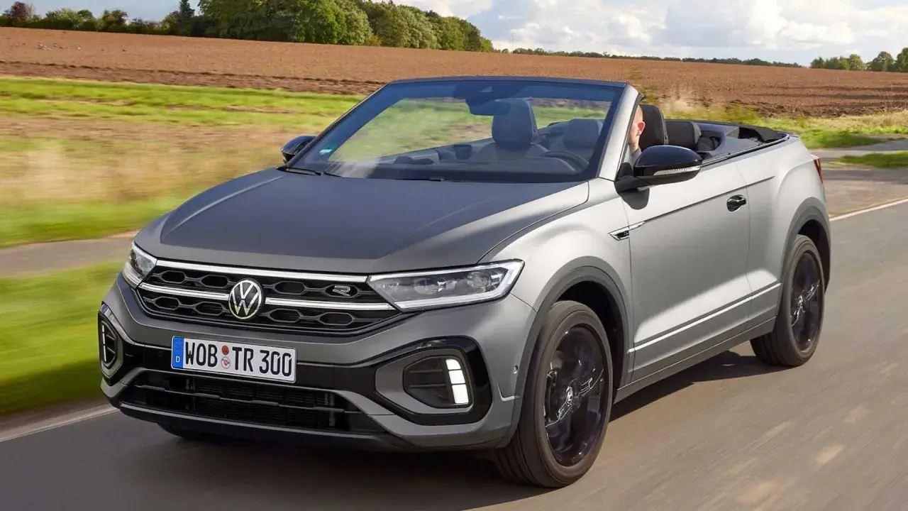 Szary Volkswagen T-Roc Cabrio jedzie po drodze, z otwartym dachem, w słoneczny dzień.