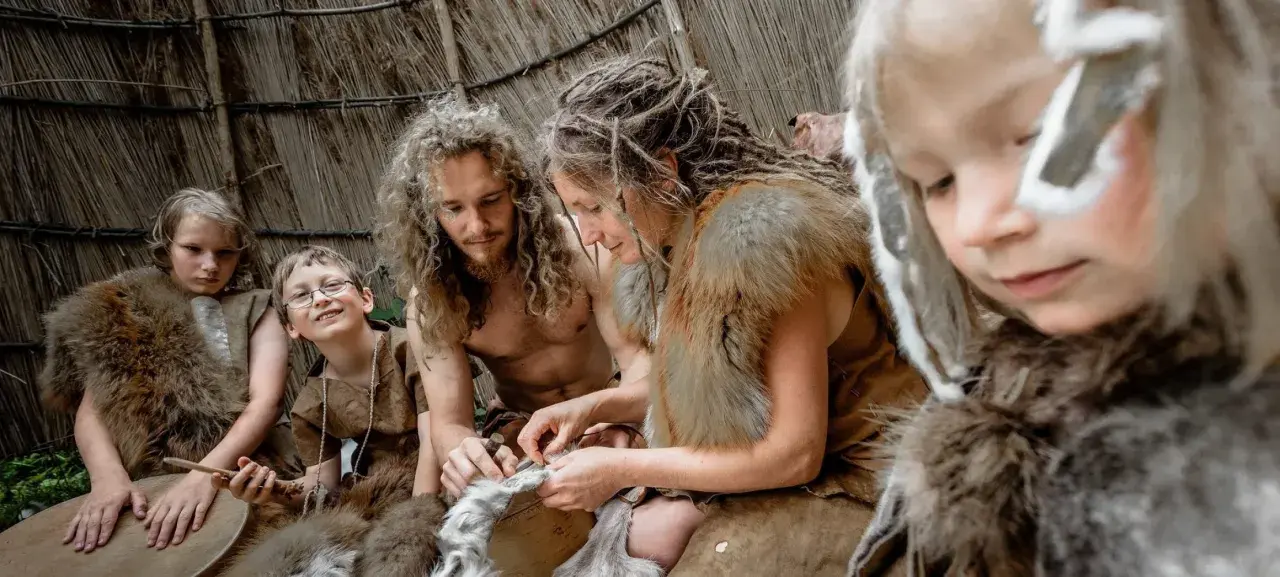 Familie in Fellkleidung übt das Ledergerben, eine lebendige Lektion für die Steinzeit Grundschule.