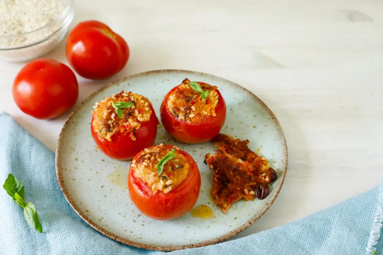 Pomodori ripieni tonno e riso, guarniti con basilico, su un piatto con un contorno croccante.