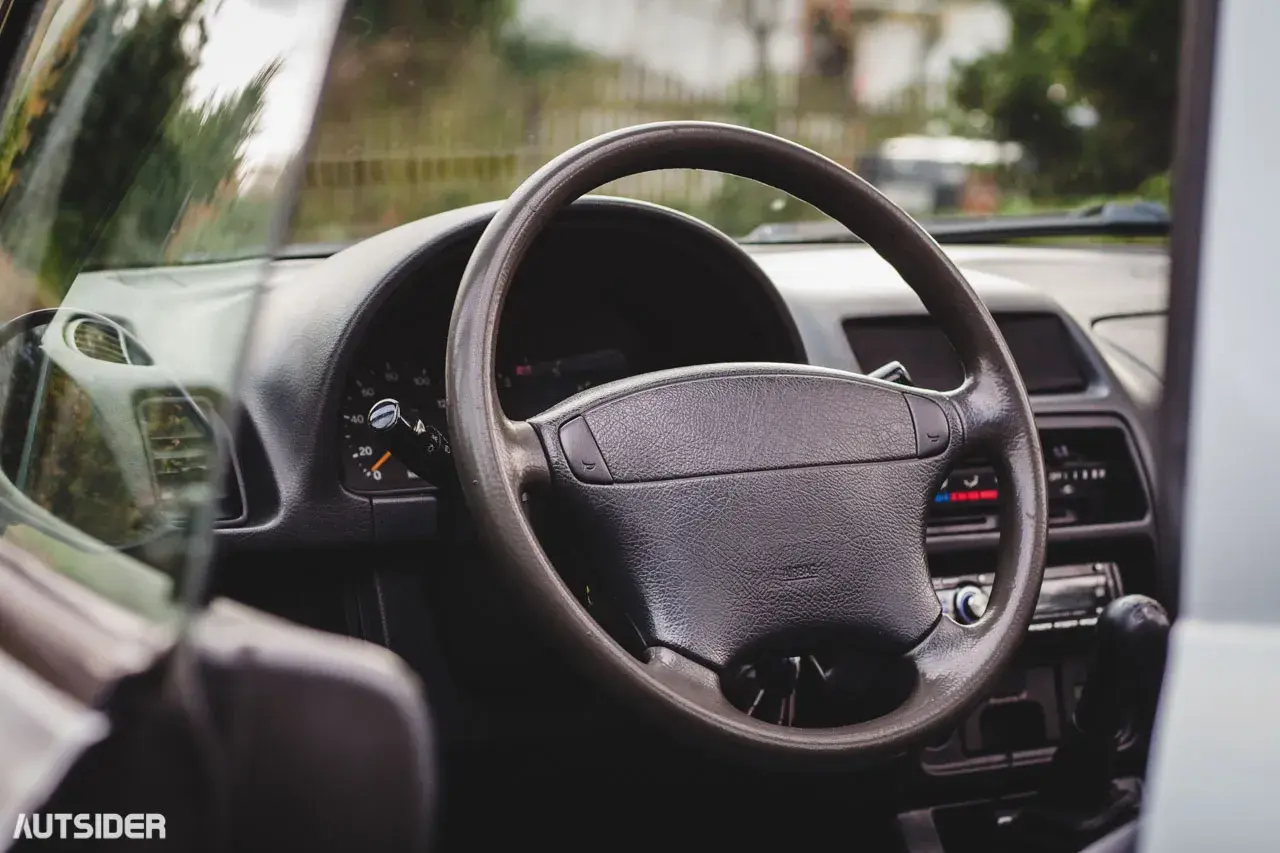 Wnętrze Suzuki X90: kierownica, deska rozdzielcza z zegarami i radiem, widok z perspektywy kierowcy.