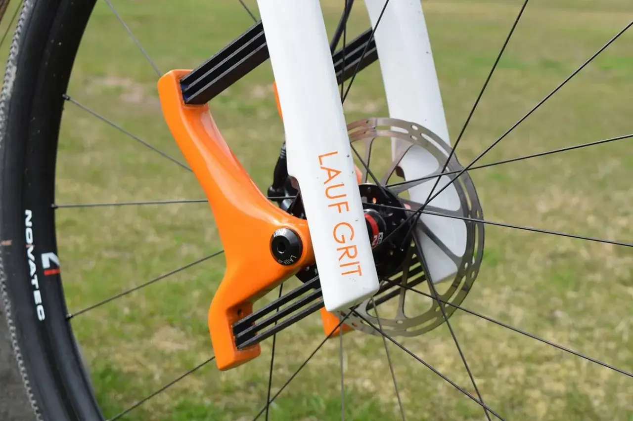 Close-up of a bright orange and white Lauf Grit fork on a bicycle wheel, ready for adventure.