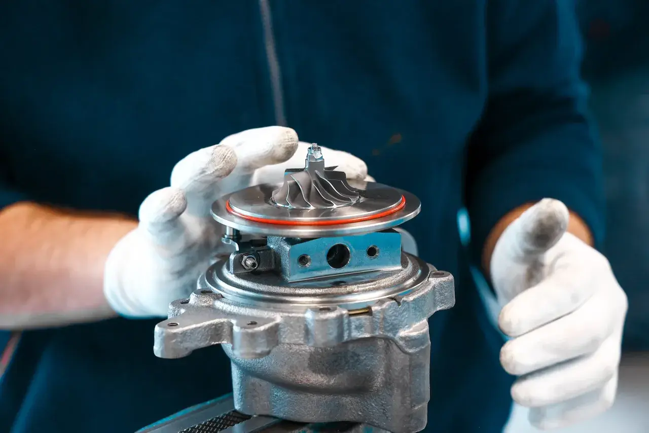 Ręce w białych rękawiczkach trzymają turbosprężarkę, gotową do montażu. To serce potężnego silnika twin turbo.