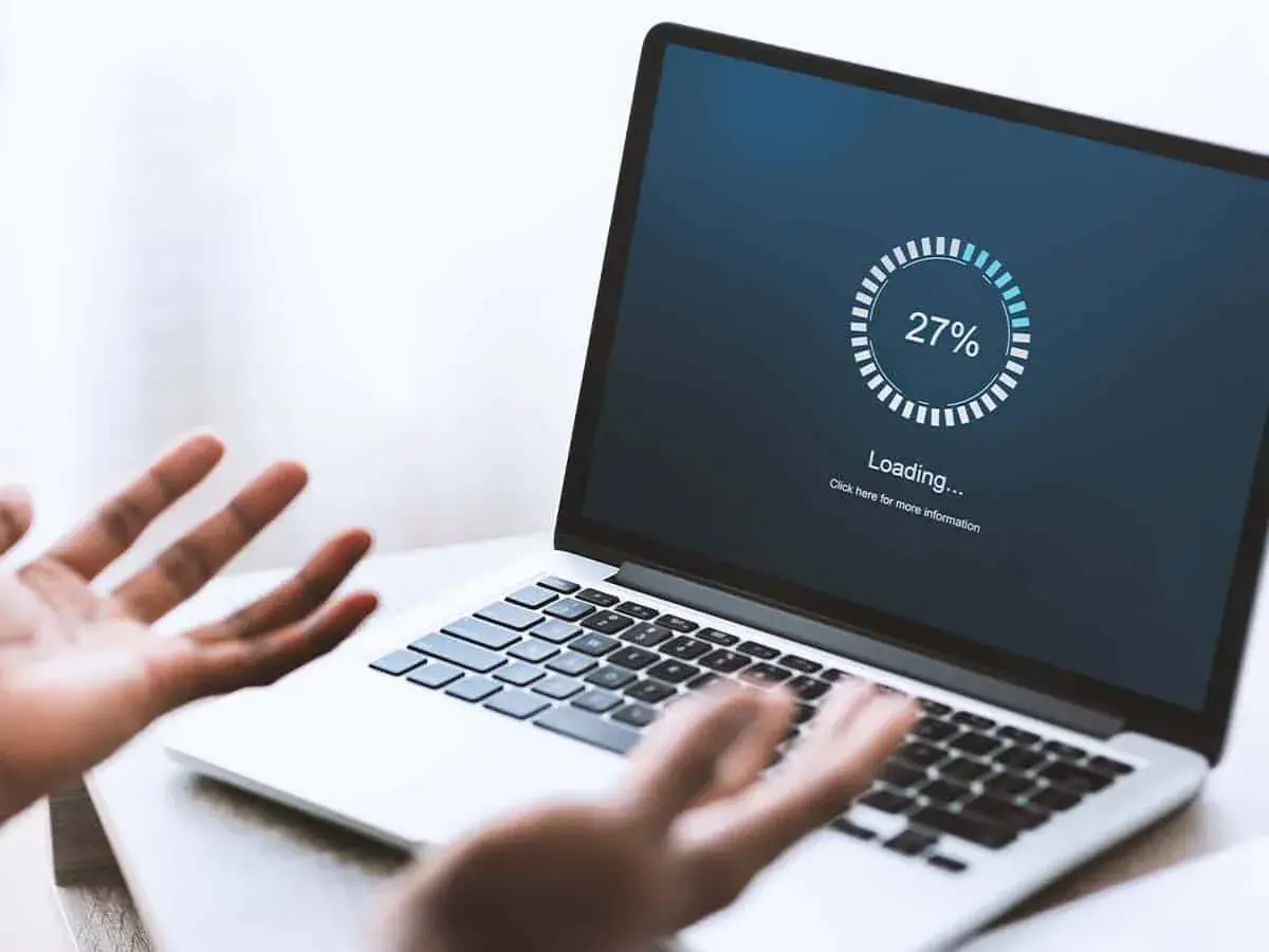 Verzweifelte Person schaut auf Laptop, auf dem "Loading... 27%" steht. Windows startet nach Update nicht mehr.