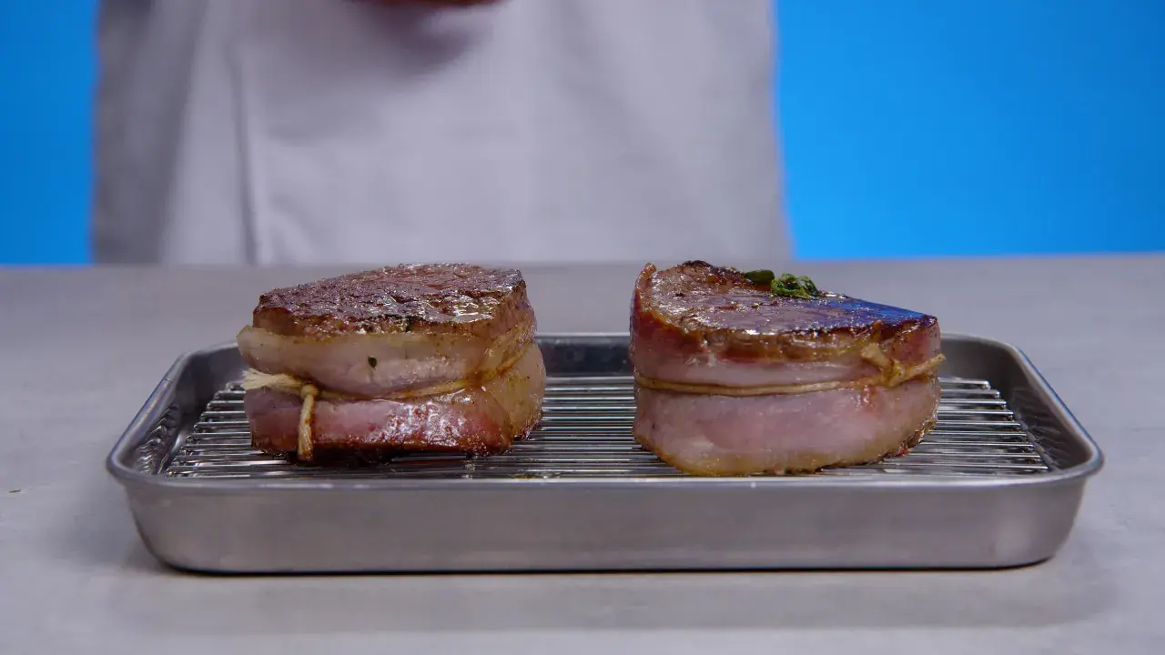 Deux filets mignons enveloppés de lard, prêts pour la cuisson, sur une grille dans un plat.
