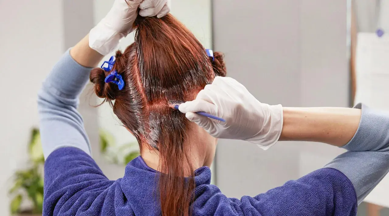 Persona se tiñe el pelo en casa, aplicando tinte con un pincel.