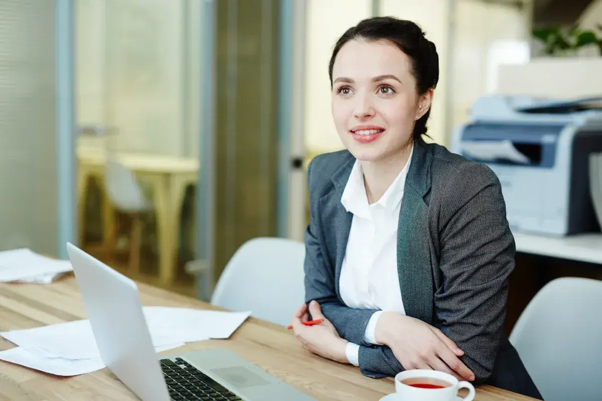 Una consulente HR sorride mentre lavora al suo laptop, analizzando dati e preparando strategie per il personale.