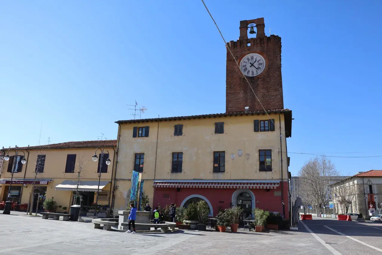 Torre dell'orologio in un tranquillo cascina paese, con negozi e gente che passeggia nella piazza.