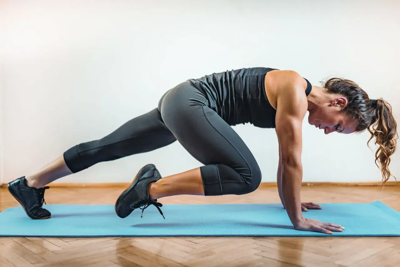 Kobieta wykonuje ćwiczenie w stylu hiit, co to za trening? Dynamiczne ruchy na macie, budowanie siły i wytrzymałości.