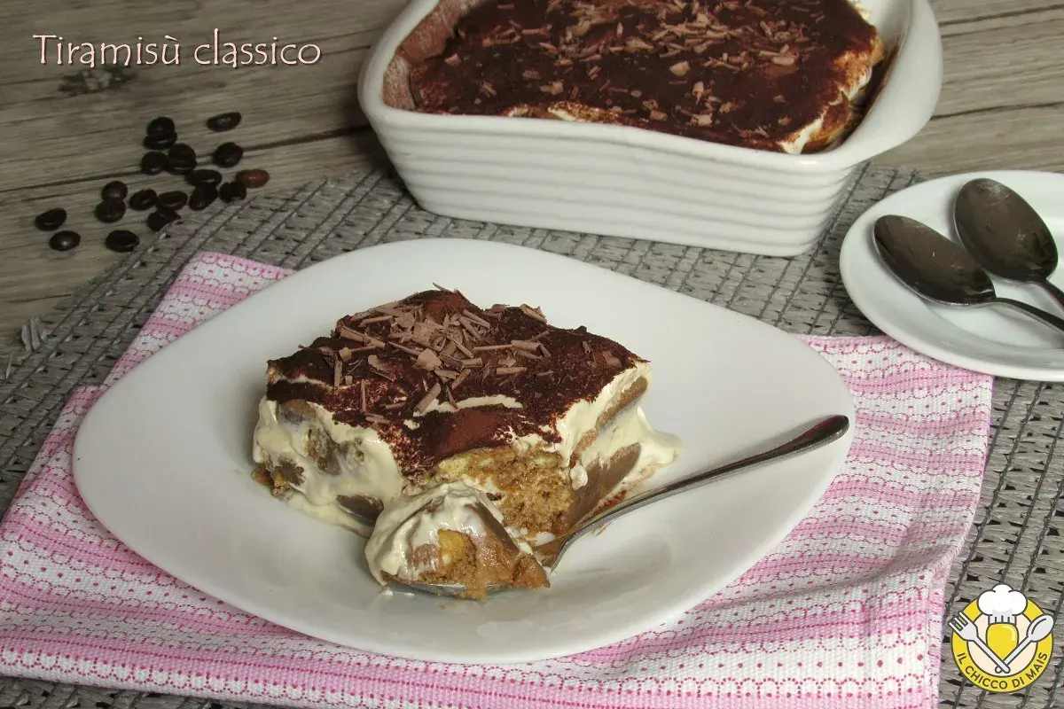 Una fetta di tiramisù classico, con savoiardi inzuppati nel caffè e crema al mascarpone, spolverato di cacao e scaglie di cioccolato. La ricetta del tiramisù è un classico intramontabile.
