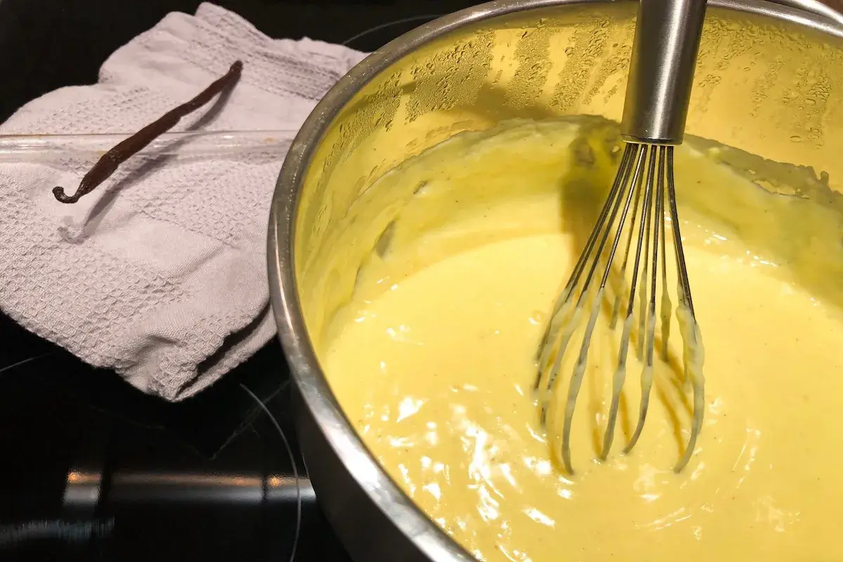 Crema pasticcera senza latte in preparazione, con bacca di vaniglia e frusta.