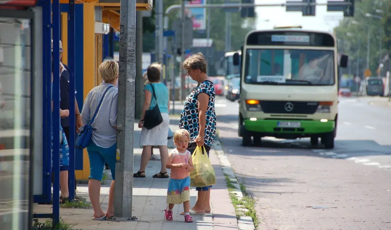 Ludzie czekający na autobus na przystanku, w tle autobus.