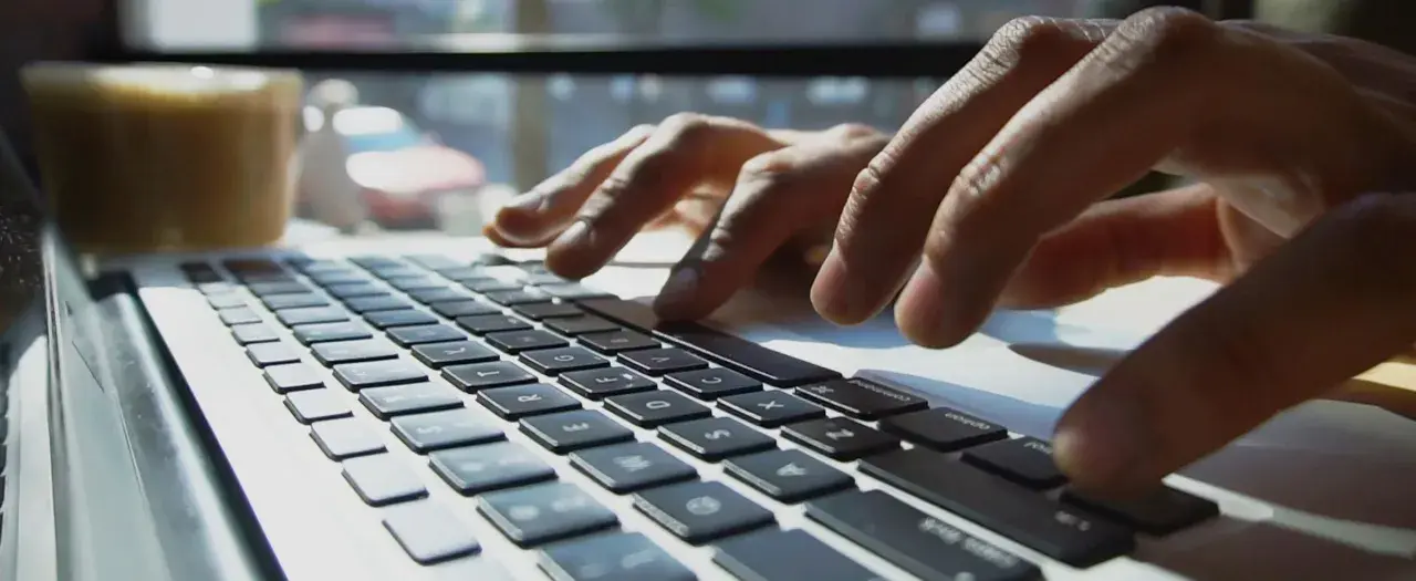 Mains sur un clavier d'ordinateur portable, une tasse de café à proximité. L'utilisateur interagit avec un chatbot helpdesk pour obtenir de l'aide.