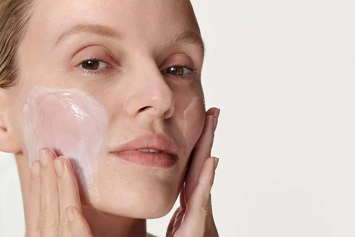 Donna applica una crema idratante sul viso. La sua pelle appare luminosa e sana, pronta per il giorno. Prima scrub o detergente? La scelta è tua per una pelle perfetta.