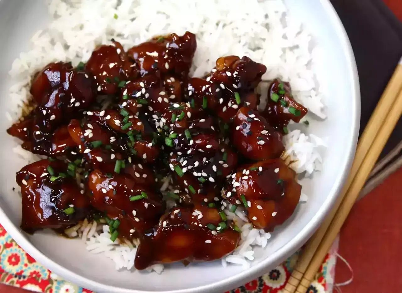 En skål med fluffigt ris toppad med glaserad teriyaki kyckling, strödd med sesamfrön och gräslök.