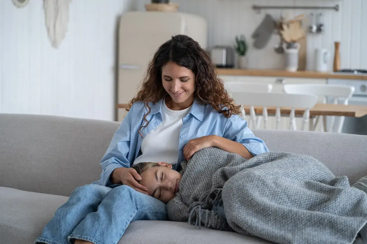 Madre reconforta a su hija, que duerme en su regazo. La menstruación a los 10 años es normal y la madre le ofrece apoyo.