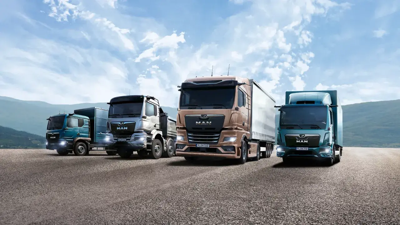 Quatre camions de la marque MAN, aux couleurs variées, roulent sur une route sous un ciel bleu nuageux.